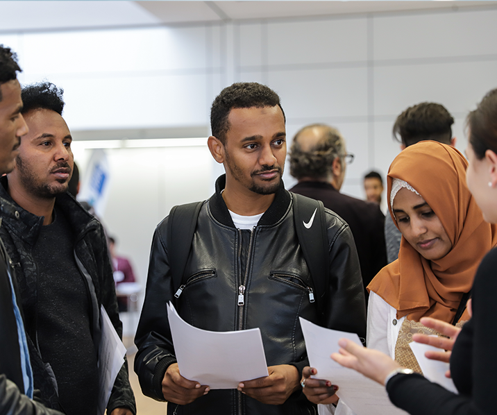 Junge Männer und eine Frau informieren sich über Berufsmöglichkeiten in Deutschland und stehen mir Informationszetteln in der Hand zusammen.