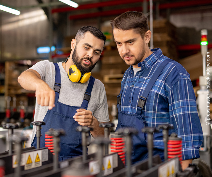 Zwei Männer stehen beratend vor einer Maschine in einer Werkshalle.
