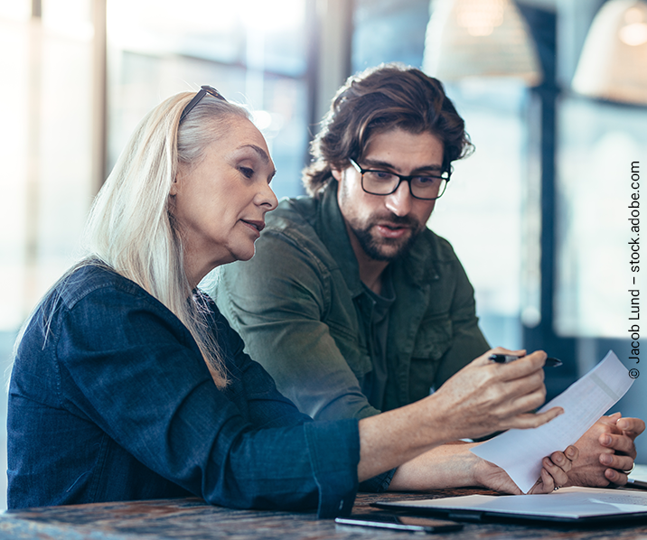 Eine Frau und ein Mann sitzen gemeinsam an einem Schreibtisch und beraten über ein Stück Papier in den Händen der Frau.