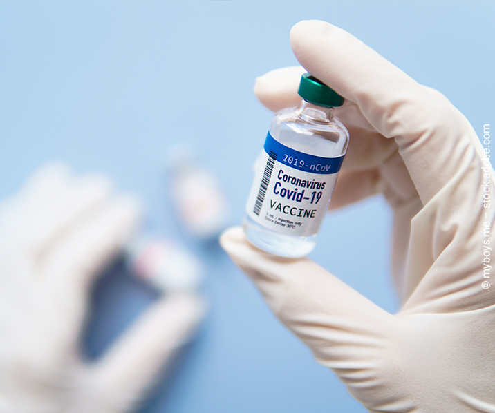 Eine Hand mit weißem Gummihandschuh hält ein Fläschchen des Covid-Impfstoffes. 