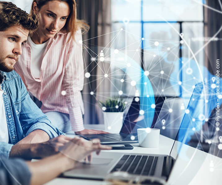 Junge Frau und Mann arbeiten an zwei Laptops über denen sich ein digitales Netzwerk öffnet