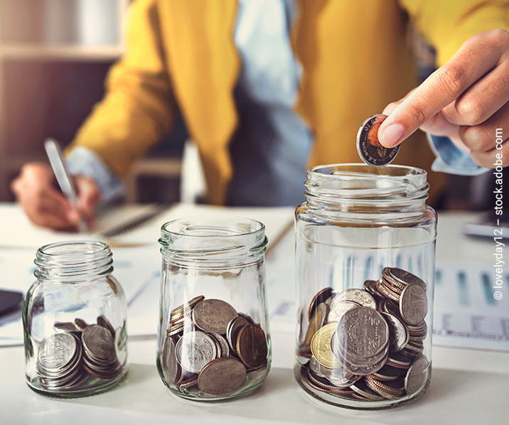 Hand lässt eine Münze in eins von drei Gläsern fallen.