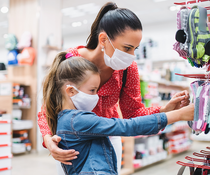 Frau mit Tochter schauen sich Kleidung an einem Ständer an. Beide tragen einen Mundschutz.