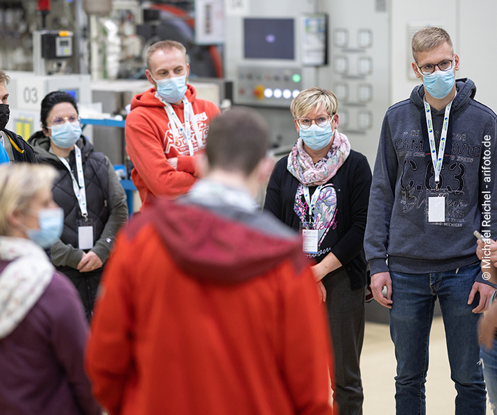 Besucher stehen in einer Fabrikhalle im Kreis und lassen sich die Funktion der Maschinen erklären.