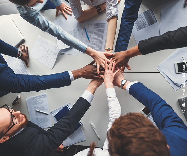 Hände von mehreren Personen, die im Kreis stehen, werden aufeinander gelegt. 