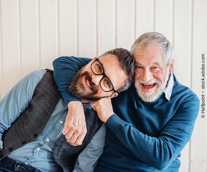 Zwei Männer aus zwei Generationen umarmen sich mit Blick in die Kamera.